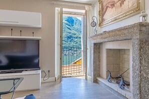 A room with a TV, a fireplace, a balcony with a view of a mountain, and a painting on the wall.