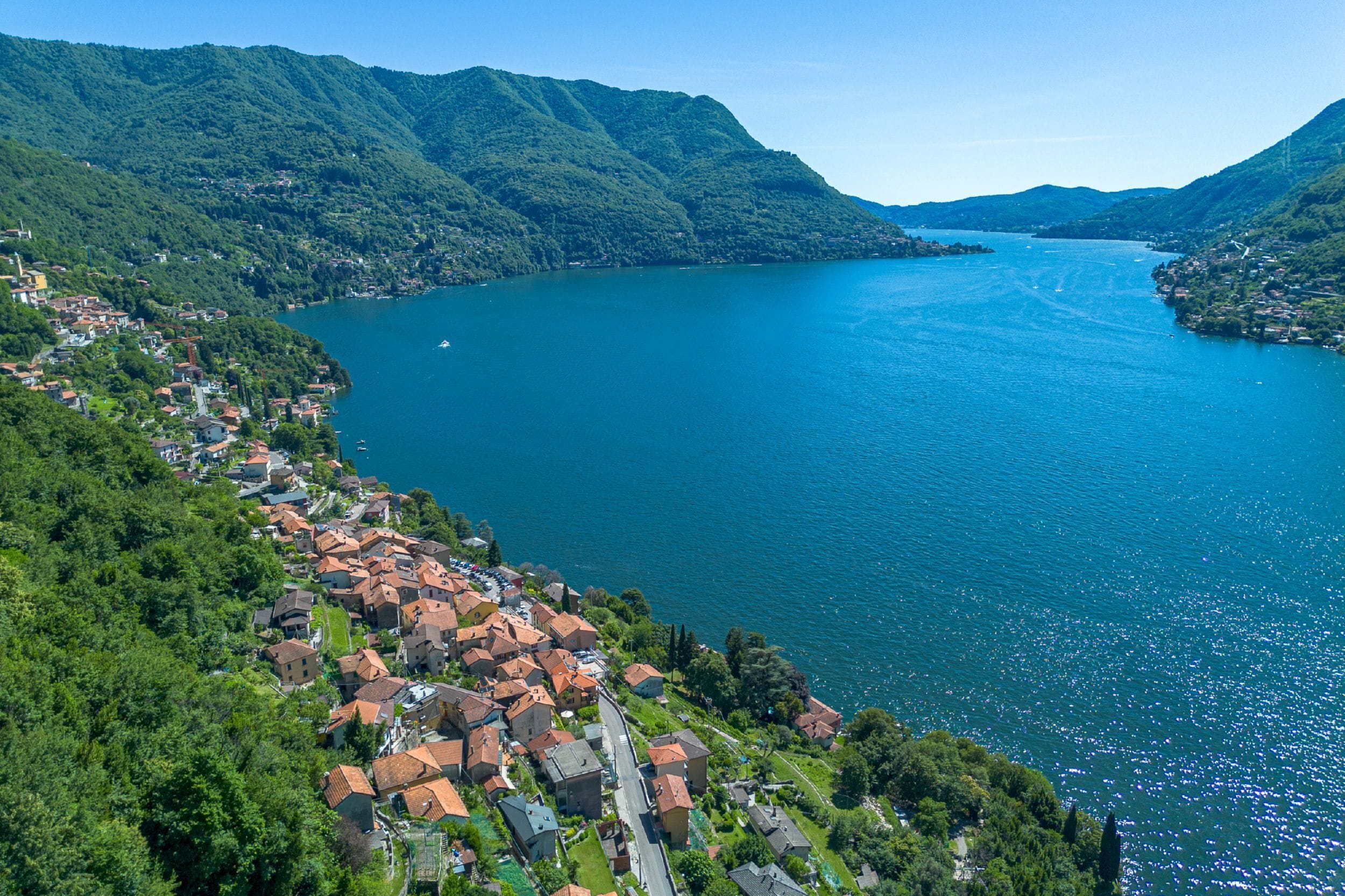 Une ville côtière avec des maisons à étages le long de la côte, un ciel dégagé et des montagnes en arrière-plan.