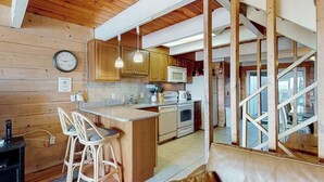 A kitchen with wooden cabinets, a microwave, a stove, and a bar area with stools. - Beach Place N 3 (Ocean City)