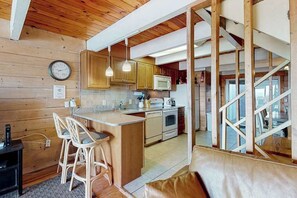 Une cuisine avec des meubles de rangement en bois, un four à micro-ondes, une cuisinière et un coin bar avec des tabourets.