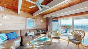 A cozy living room with a wooden ceiling, a ceiling fan, a glass coffee table, a brown leather sofa, and a large window with a view. - Beach Place N 3 (Ocean City)