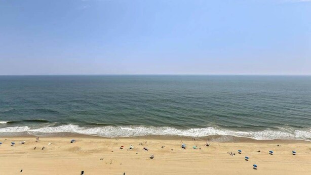 Een strand met heldere lucht, rustige zee en mensen in het zand.