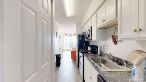 A kitchen with white cabinets, a black stove, a sink, and a marble countertop. - Assateague House 511 (Ocean City)