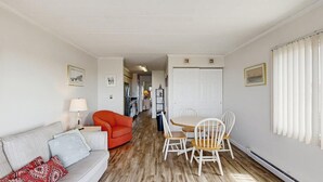 A room with a sofa, a dining table with chairs, a red chair, a lamp, and a picture on the wall. - Assateague House 511 (Ocean City)