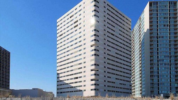 A tall, modern building with a grid of windows, surrounded by a sandy area with sparse vegetation. - Well-Appointed Vacation Getaway in Oceanfront Complex w/Shared Pool, Free WiFi (Ocean City)