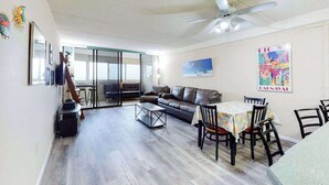 A spacious living area with a sofa, a dining table with chairs, a ceiling fan, and a large window. - Well-Appointed Vacation Getaway in Oceanfront Complex w/Shared Pool, Free WiFi (Ocean City)