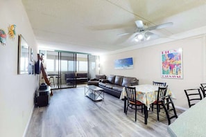 A spacious living area with a sofa, a dining table with chairs, a ceiling fan, and a large window. - Well-Appointed Vacation Getaway in Oceanfront Complex w/Shared Pool, Free WiFi (Ocean City)