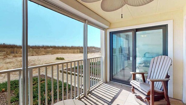 Ein Balkon mit Blick auf den Strand, eine Glastür und ein Deckenventilator.