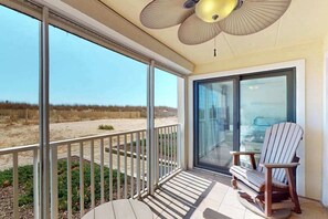 A balcony with a view of the beach, a glass door, and a ceiling fan. - Anchorage II 107 (Ocean City)