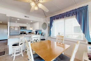 Eine moderne Küche mit weißen Schränken, einer zentralen Kochinsel und einem Essbereich mit Holztisch und weißen Stühlen.