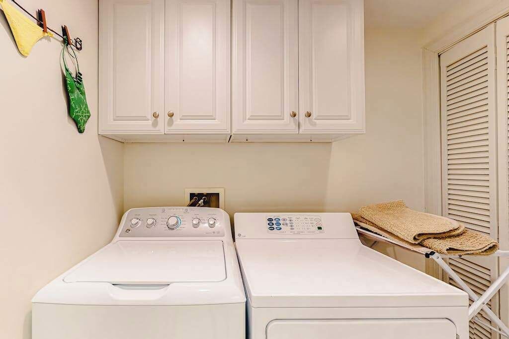 Un espace buanderie équipé de deux machines à laver et deux sèche-linge, d’un étendoir et de placards blancs situés en hauteur.