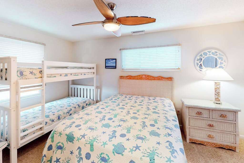 A child's bedroom with bunk beds, a ceiling fan, a bedside lamp, and a window with blinds.