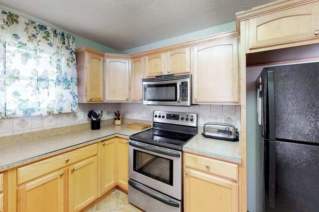 A kitchen with wooden cabinets, a stainless steel oven, a microwave, a toaster, and a black refrigerator.