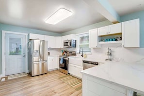 A modern kitchen with white cabinets, stainless steel appliances, and a marble countertop.