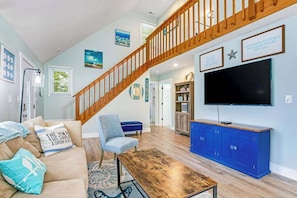 A living room with a wooden staircase, a television, a blue cabinet, and a sofa with decorative pillows.