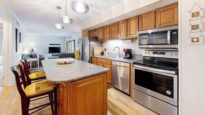 A modern kitchen with wooden cabinets, stainless steel appliances, and a central island with bar stools. - Oceanfront Tide's Edge condo with balcony & boardwalk - walkable locale (Ocean City)