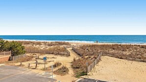 A beach view with a parking area, a pathway leading to the beach, and a fence. - Oceanfront Tide's Edge condo with balcony & boardwalk - walkable locale (Ocean City)