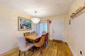 Ein Esszimmer mit Holztisch, Korbstühlen, einer Chandelierleuchtre und einem Gemälde an der Wand.