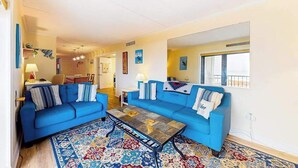 A living room with two blue sofas, a coffee table, and a patterned rug. - Oceanfront Tide's Edge condo with balcony & boardwalk - walkable locale (Ocean City)