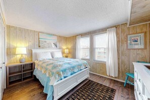 Ein Schlafzimmer mit einem Bett, Nachttischlampen, einer Holzwand, einem Fenster mit Vorhängen und einem Bilderrahmen.