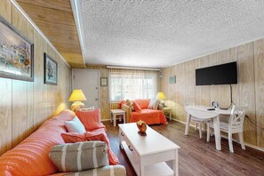 Ein gemütliches Zimmer mit Holzwand, einer Couch, einem Esstisch und einem an der Wand befestigten Fernseher.