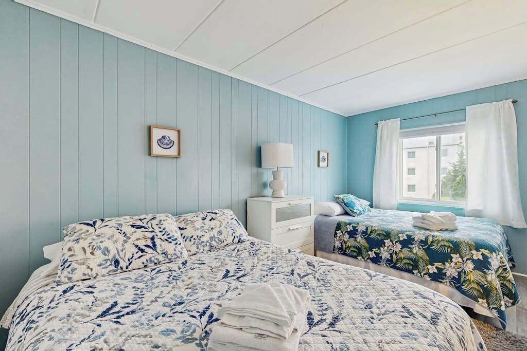 A bedroom with two beds, a nightstand, a lamp, and a window with curtains.