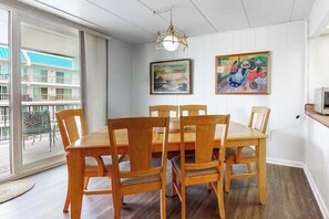 A dining area with a wooden table and chairs, a chandelier, and two paintings on the wall. - 3rd-floor condo near the beach with balcony, partial ocean views, & central AC (Ocean City)