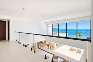 A spacious balcony with a clear view of the ocean and a pool area with lounge chairs. - Beachfront 6BR Pool Villa | Private Chef, Butler | TipSea Villa by Bocobay (St. Ann’s Bay)