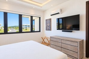 Ein modernes Schlafzimmer mit einem großen Bett, einem an der Wand montierten Fernseher und Blick auf ein Gebäude durch ein großes Fenster.