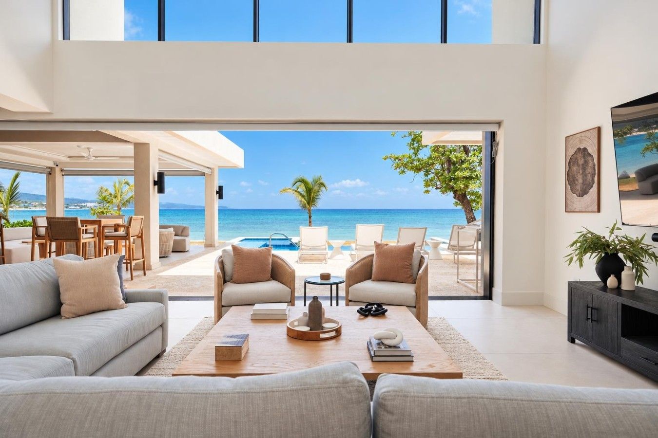 A modern living room with a large window overlooking a beach, furnished with sofas, chairs, and a coffee table.
