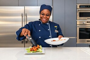 Un chef, vêtu d’un uniforme, verse une sauce sur des aliments dans une cuisine équipée d’appareils en acier inoxydable.