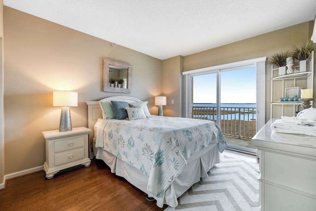 A bedroom with a bed, nightstands, a dresser, a large window with a view, and a mirror.