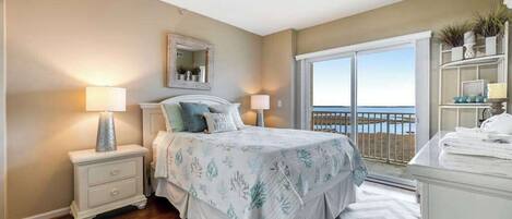 A bedroom with a bed, nightstands, a dresser, a large window with a view, and a mirror.
