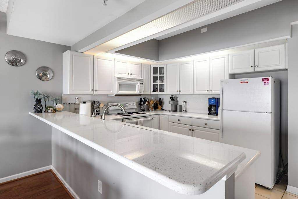 A modern kitchen with white cabinetry, a large island, stainless steel appliances, and a grey wall.