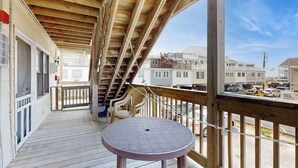 En overdækket terrasse med et rundt bord og stole, trægelændere og udsigt til omkringliggende huse.