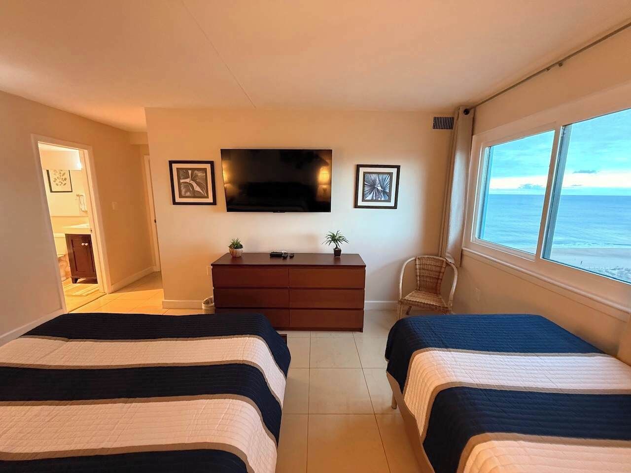 Une chambre d’hôtel avec deux lits, une télévision, une commode, une chaise et une vue sur la mer.