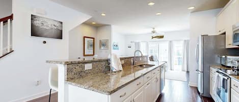 A spacious kitchen with a granite countertop, white cabinetry, and stainless steel appliances.