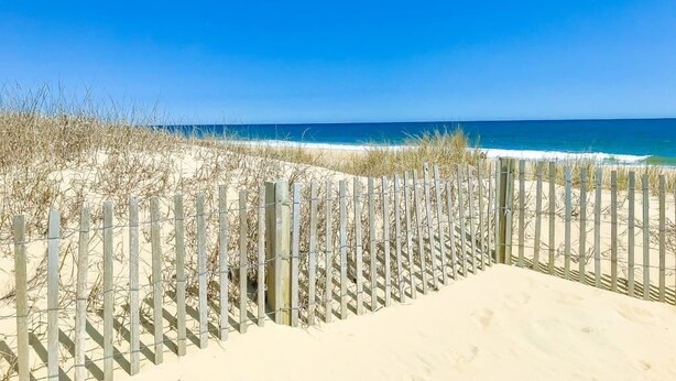 Ein Strand mit einer Holzlattenzäunung und Dünen.