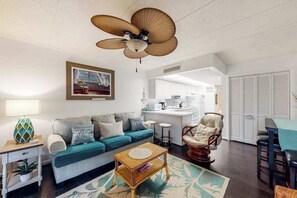 A living room with a sofa, a coffee table, a chair, a ceiling fan, a kitchen area, and a dining table. - Beach House 202, ocean view & balcony (Ocean City)