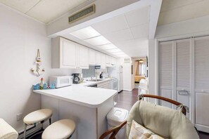 A compact kitchen with white cabinets, a central island, and a small seating area. - Beach House 202, ocean view & balcony (Ocean City)