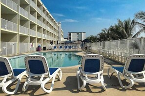 A poolside area with lounge chairs, a swimming pool, and a building with balconies. - Beautiful beachfront condo with pools, ice rink, arcade, gym, & fast WiFi (Ocean City)