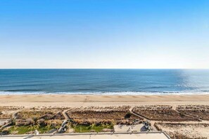A beach view with a sandy area, a pathway, and a building in the foreground. - Beautiful beachfront condo with pools, ice rink, arcade, gym, & fast WiFi (Ocean City)