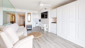 A modern living room with a sofa, a dining table, and a kitchen area with white cabinets. - Beachfront studio with balcony, AC & beachfront & rooftop pools (Ocean City)
