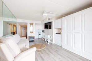 A modern living room with a sofa, a dining table, and a kitchen area with white cabinets. - Beachfront studio with balcony, AC & beachfront & rooftop pools (Ocean City)