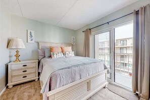 Ein Schlafzimmer mit Bett, Nachttisch, Lampe und Blick auf einen Balkon.
