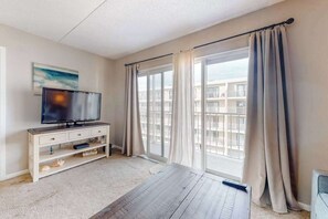Ein Zimmer mit Fernseher auf einem weißen Schrank, einem großen Fenster mit Vorhängen und Blick auf Gebäude.
