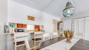A dining area with a round table, white chairs, a decorative centerpiece, and a kitchen in the background. - Wight Bay South 449 (Ocean City)