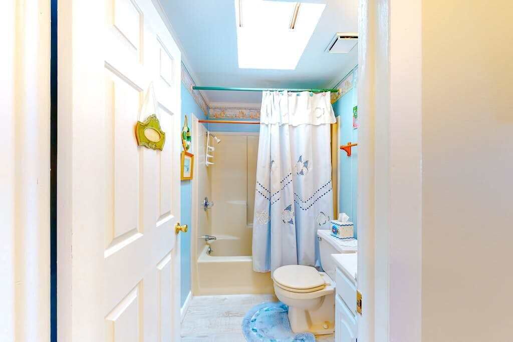 A narrow bathroom with a bathtub, toilet, and shower curtain.