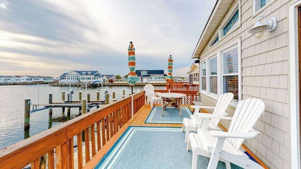 A deck with white chairs and a table, overlooking a marina with boats and colorful towers. - Canal front home with free WiFi, deck, private dock, shared pool & tennis (Ocean City)
