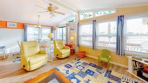 A living room with a ceiling fan, a yellow sofa, a green chair, a patterned rug, and a bookshelf. - Canal front home with free WiFi, deck, private dock, shared pool & tennis (Ocean City)